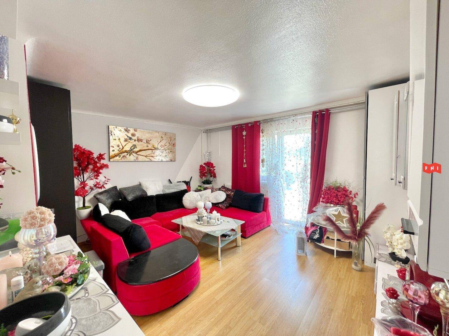 Gemütliches Wohnzimmer mit rotem Ecksofa, hellem Laminatboden und Zugang zu einem Balkon.
