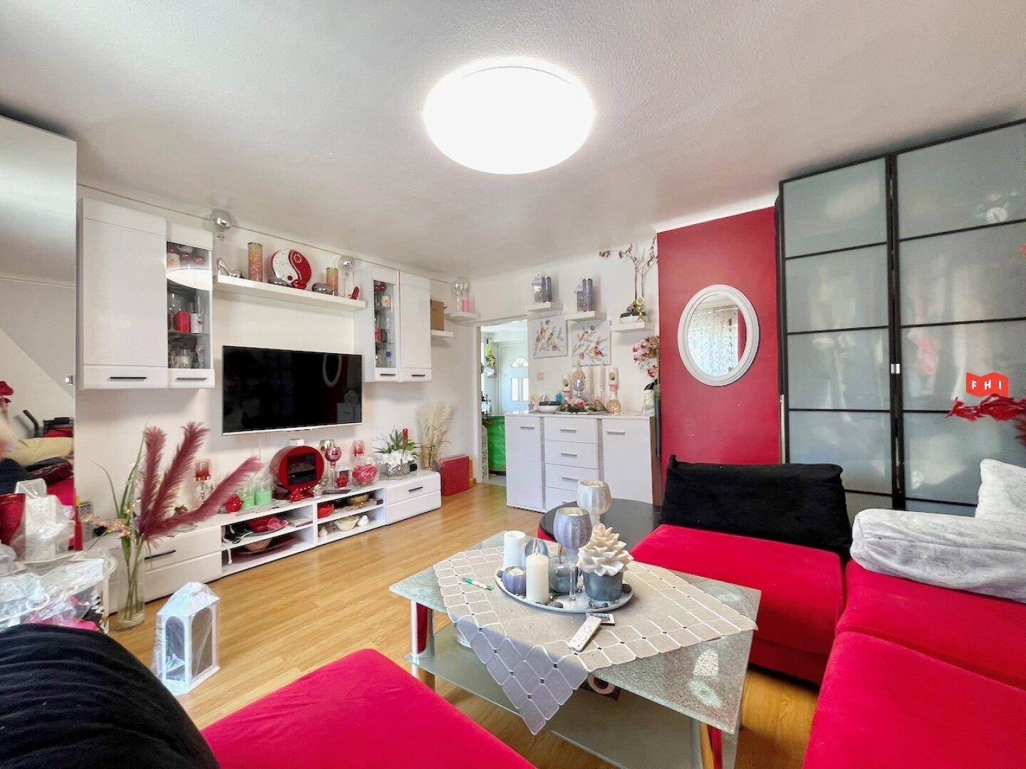 Helles Wohnzimmer mit rotem Sofa, weißer Schrankwand und einem Fernseher an der Wand.