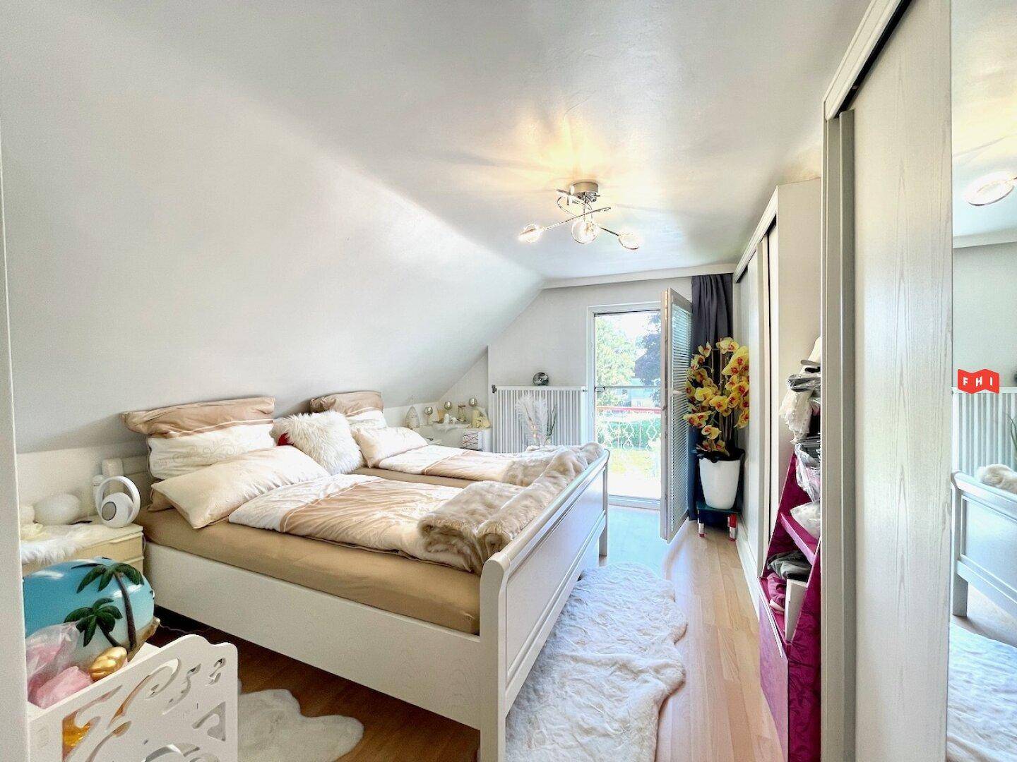 Schlafzimmer im Dachgeschoss mit zwei Betten, Laminatboden und Zugang zu einem französischen Balkon.