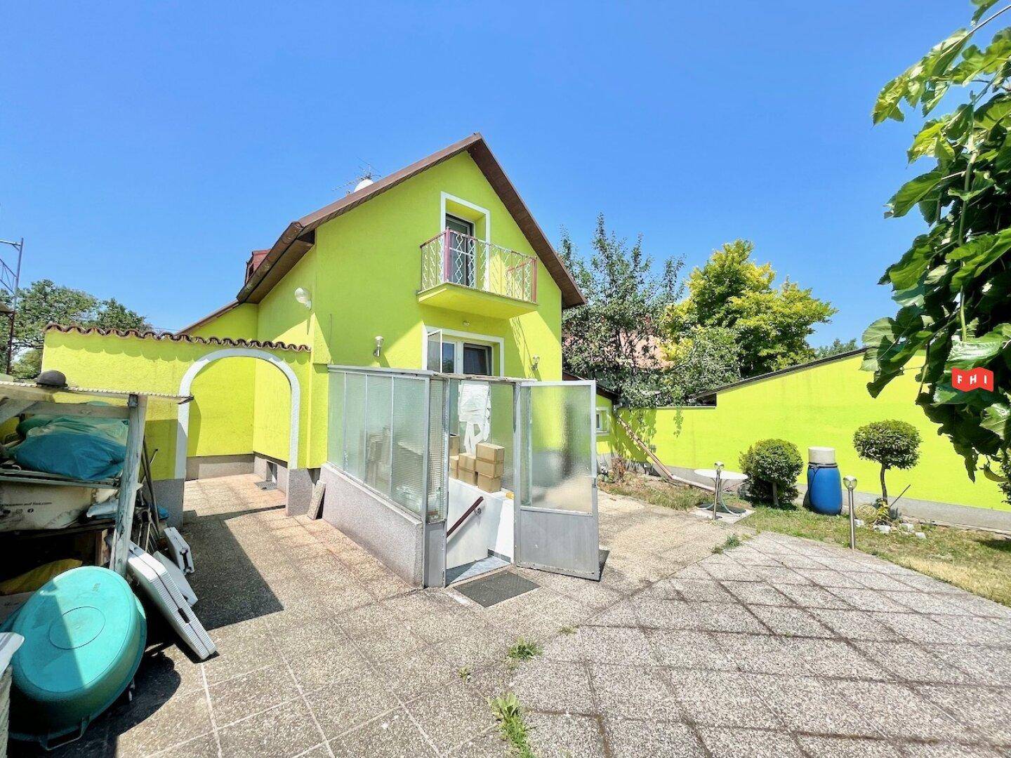 Helles, freistehendes Haus mit leuchtend grüner Fassade, kleinem Balkon und gepflastertem Außenbereich.