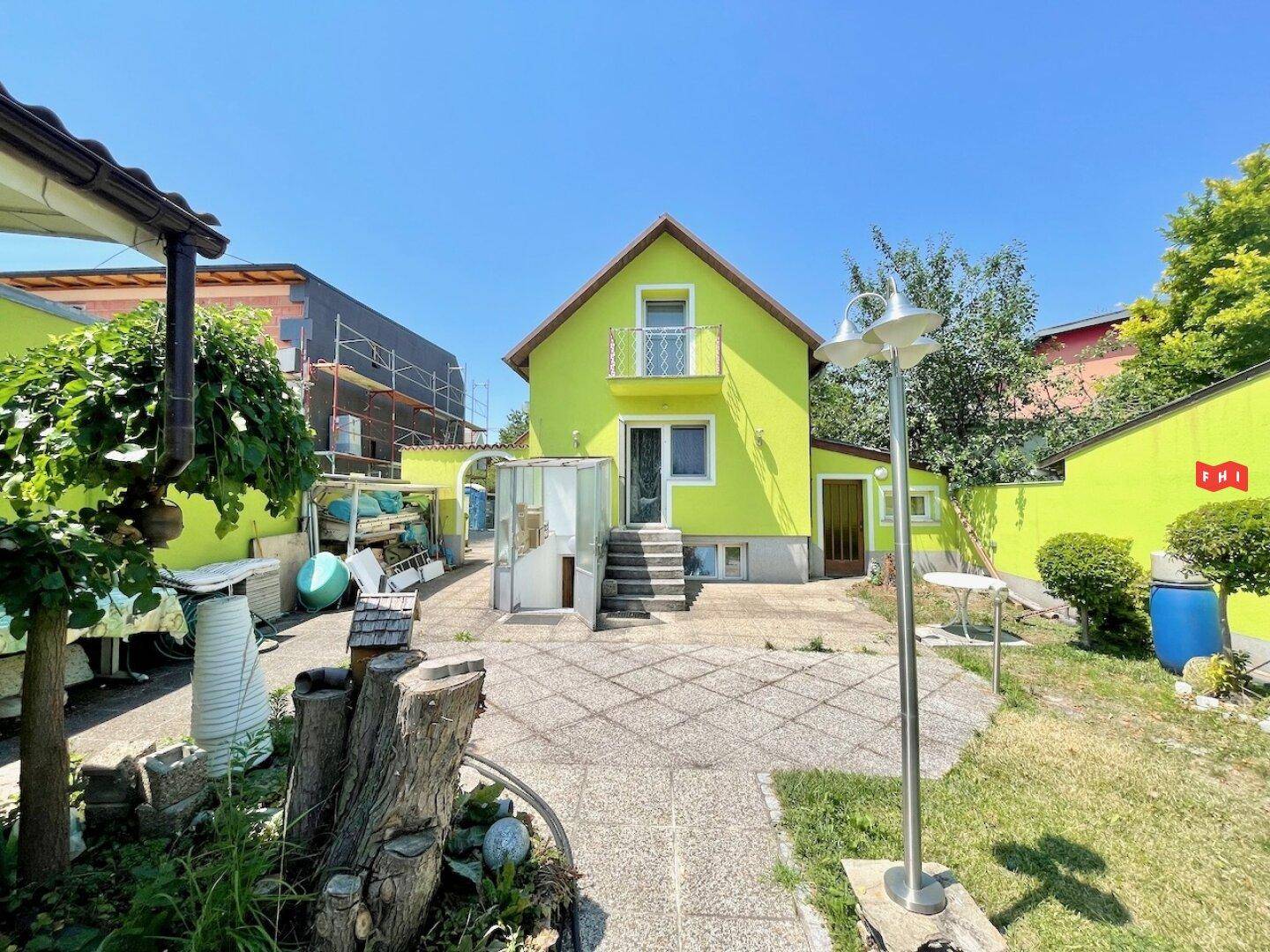 Gartenbereich hinter dem Haus mit gepflasterter Fläche, kleinem Balkon und Blick auf die Nachbarschaft.