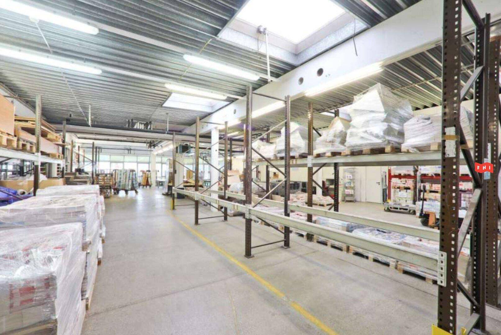 Geräumige Lagerhalle mit hohen Regalen, Oberlichtern und Betonboden für industrielle Nutzung.