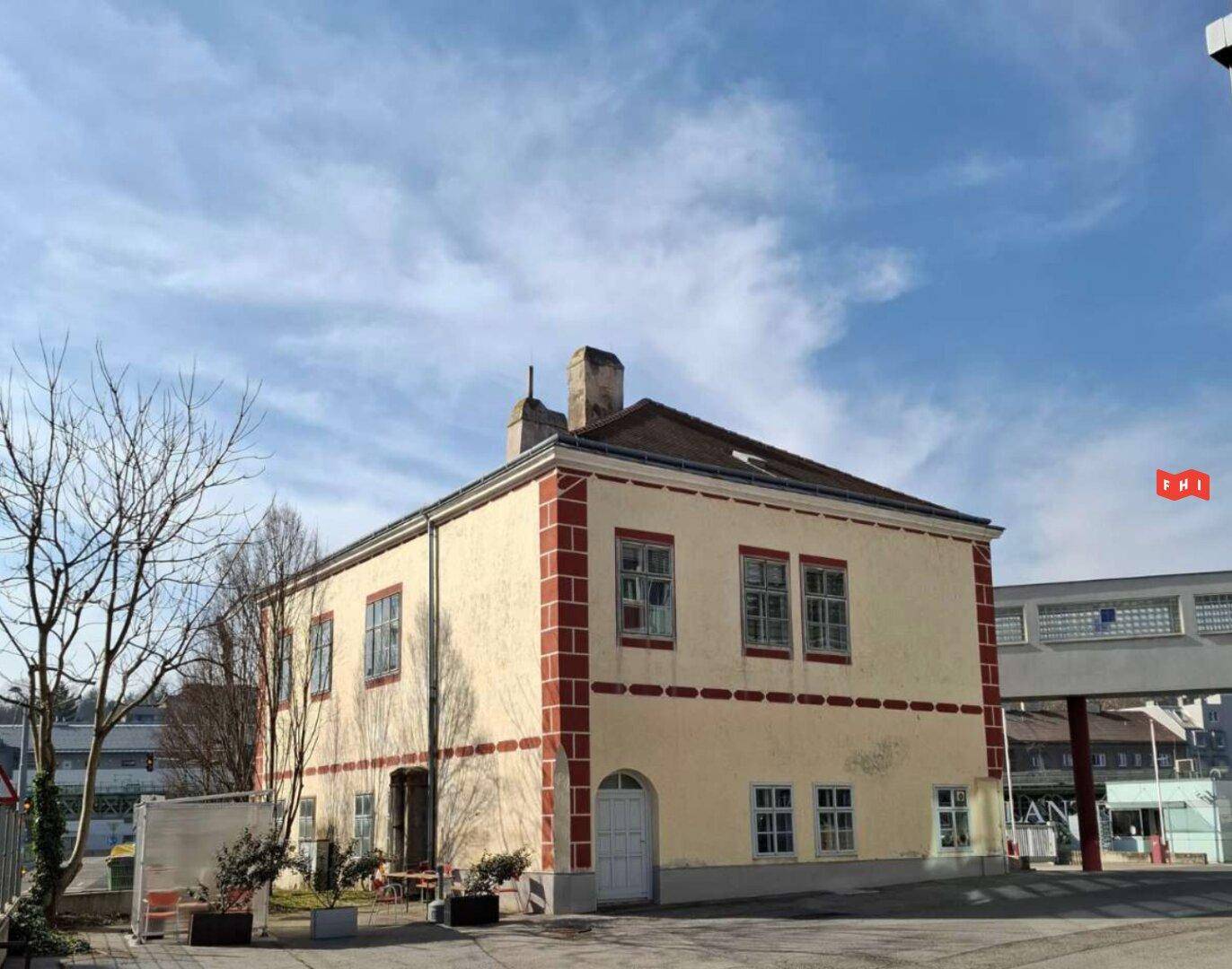 Historisches Gebäude mit gelber Fassade, roten Akzenten und traditioneller Architektur unter blauem Himmel.
