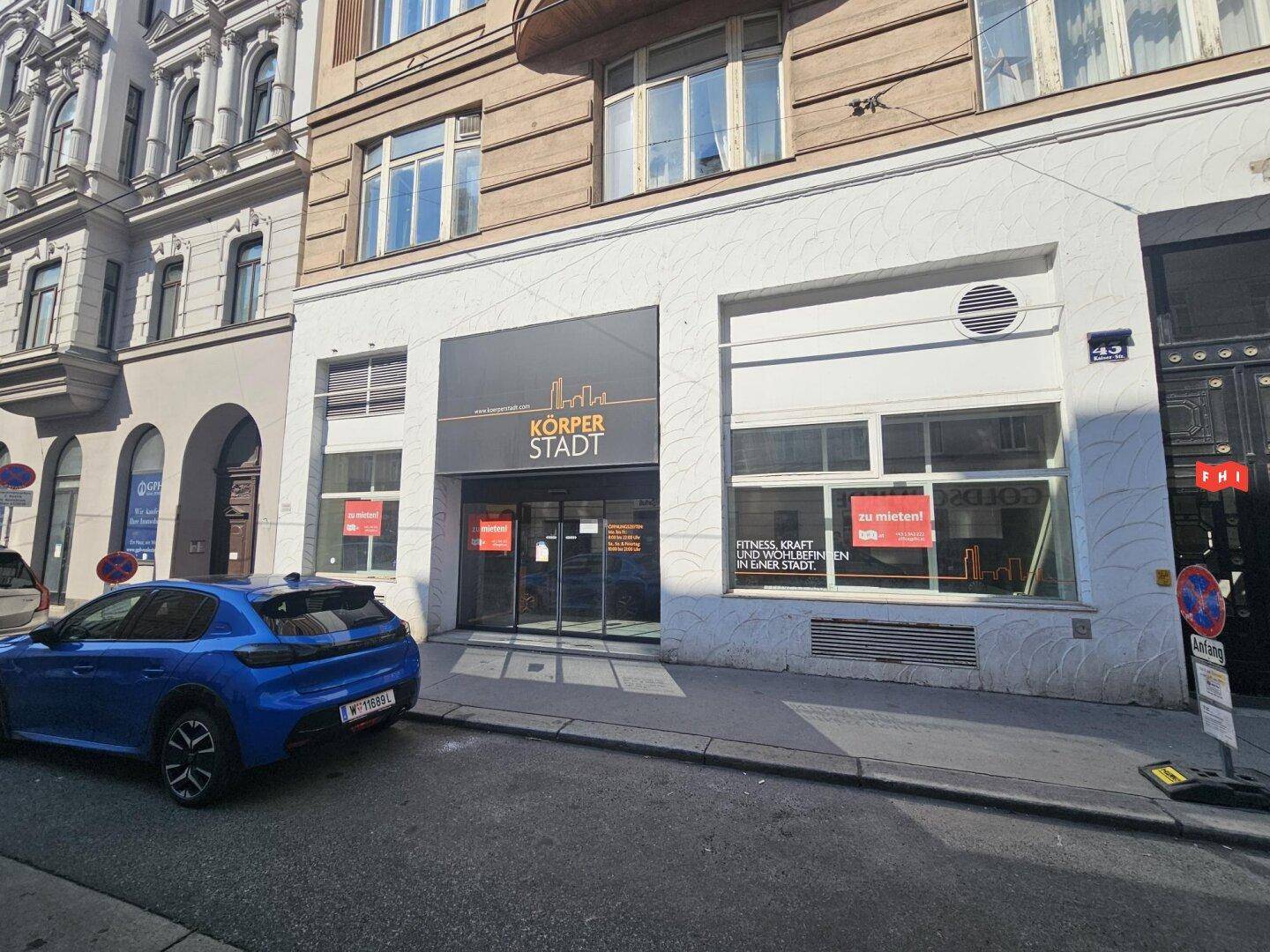 Straßenansicht eines Gebäudes mit klassischer Architektur in den oberen Stockwerken und einem modernen Geschäft im Erdgeschoss.