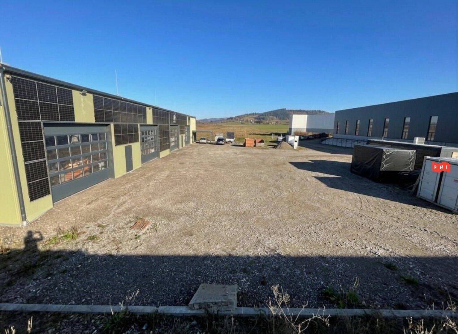 Weitläufiger Schotterbereich neben dem Gebäude mit Blick auf die hügelige Landschaft und weitere Bauten.