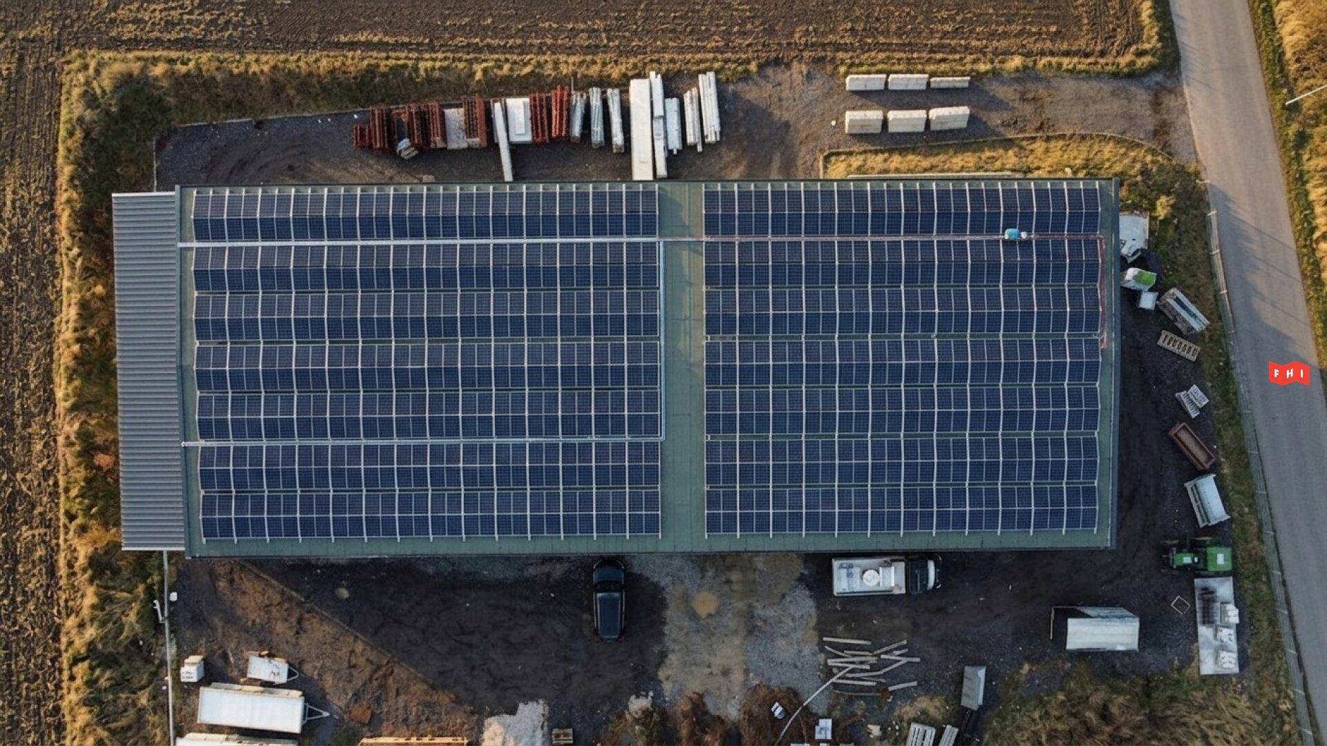 Draufsicht auf das Gewerbegebäude mit einer großen Photovoltaikanlage, umgeben von Feldern und einer Zufahrtsstraße.