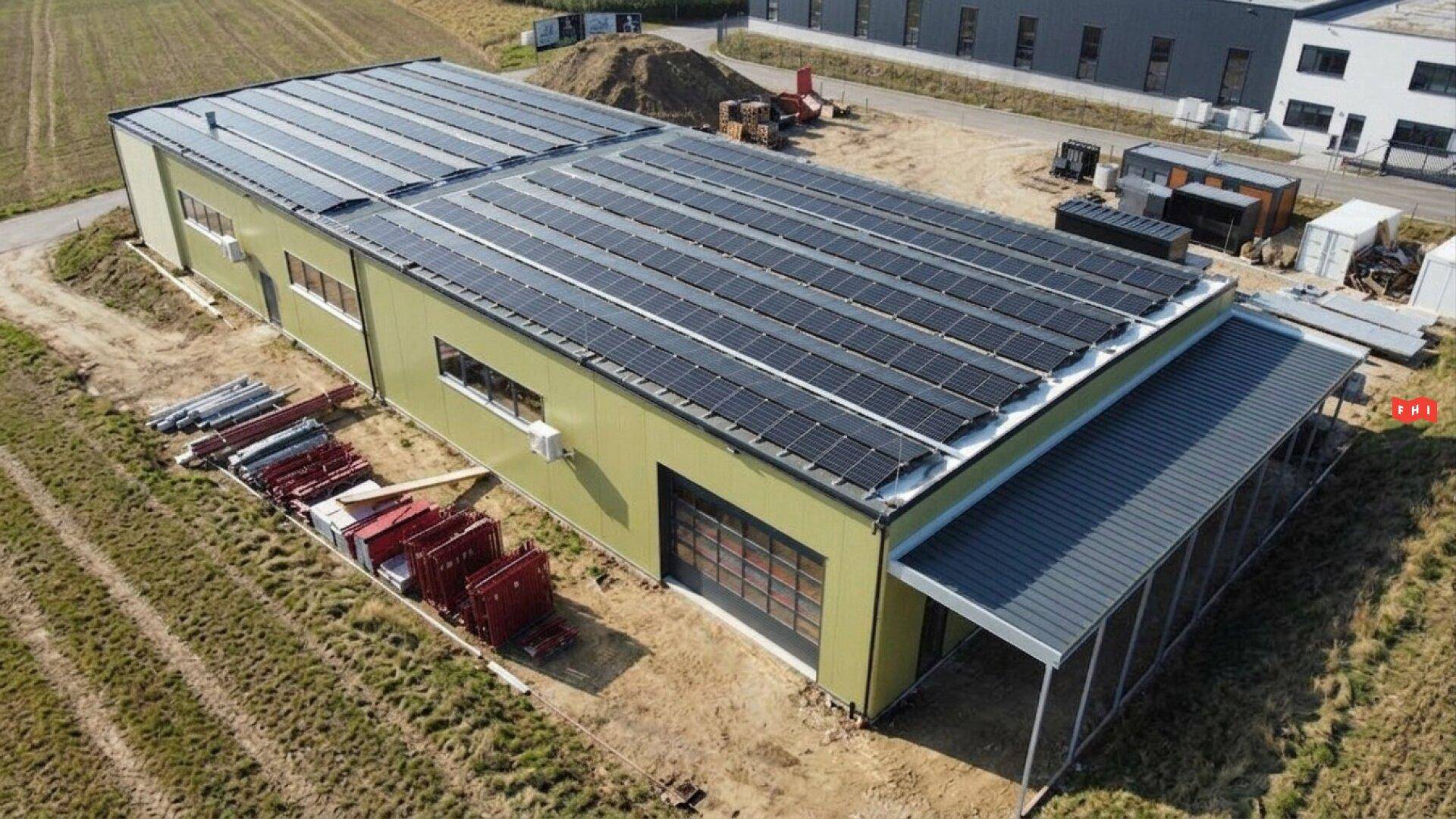 Luftaufnahme des Gewerbegebäudes mit vollständig mit Solarmodulen bedecktem Dach und umliegendem Gelände.