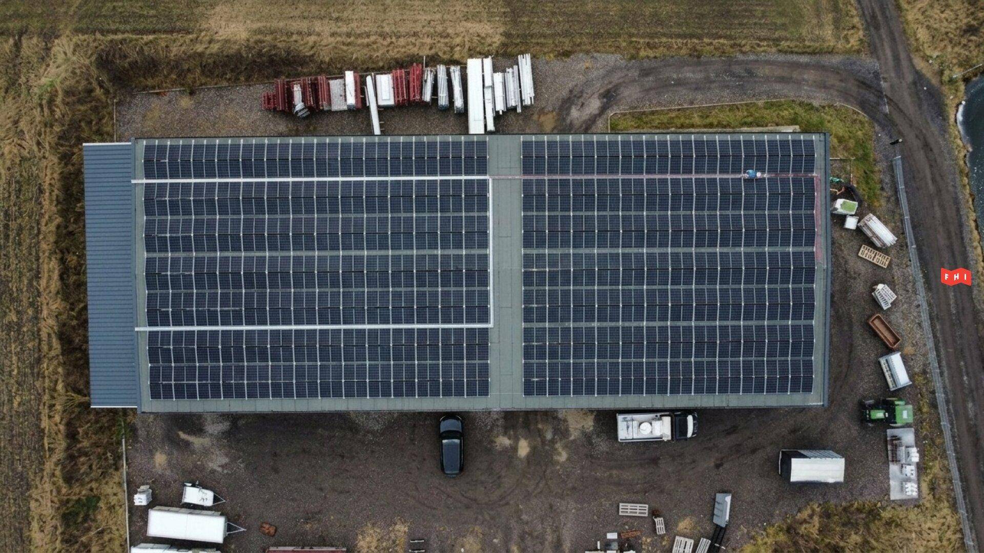 Draufsicht auf das Gewerbegebäude mit einer großen Photovoltaik-Anlage auf dem Dach und umliegendem Gelände.