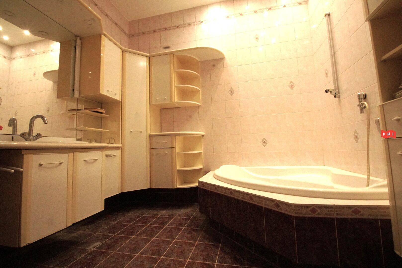 Ein Badezimmer mit Eckbadewanne, Waschtisch und Fliesen in warmen Farbtönen.