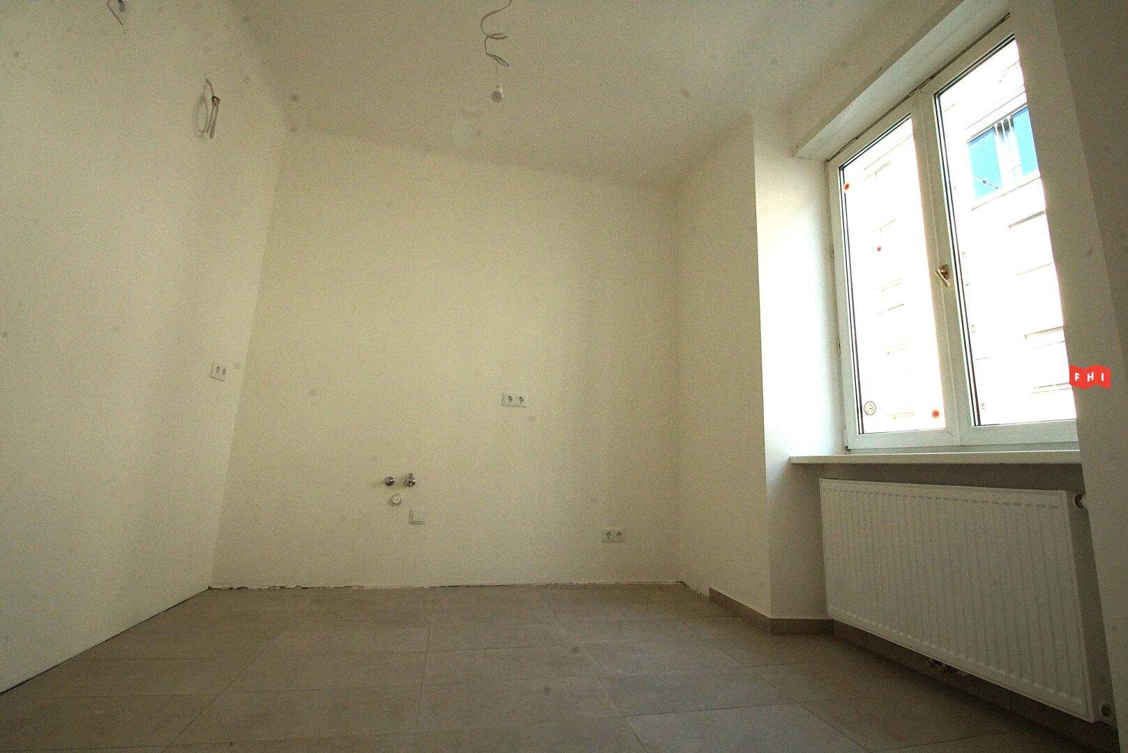 Ein Raum im Rohbau mit einem Fenster und vorbereiteten Anschlüssen, bereit für den Ausbau.