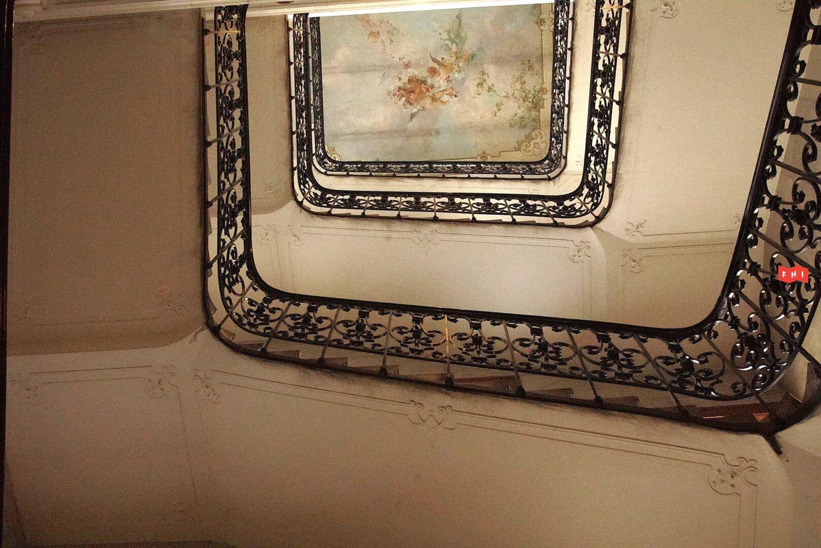 Eine elegante Wendeltreppe mit schmiedeeisernem Geländer und einem bemalten Deckengemälde.