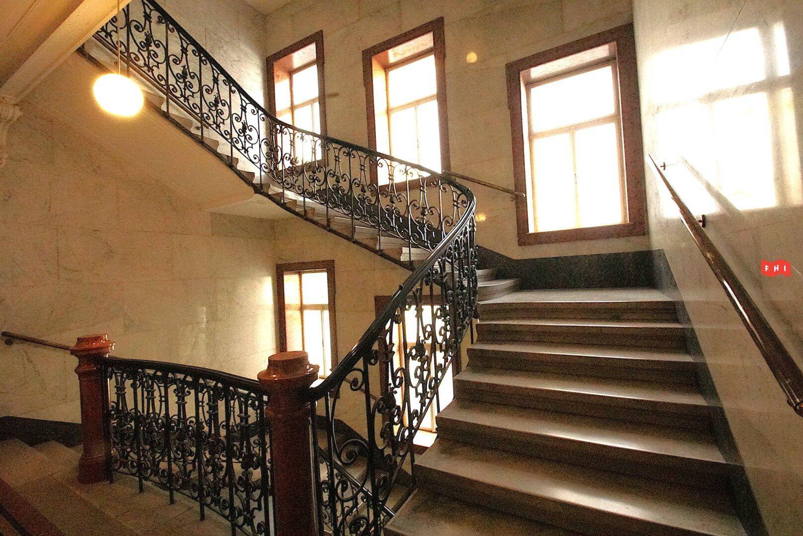 Eine beeindruckende Treppe mit Marmorwänden, schmiedeeisernem Geländer und großen Fenstern.