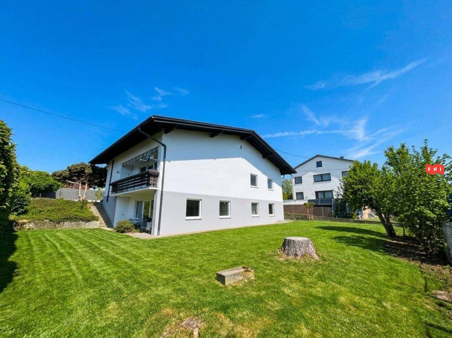 Seitenansicht des Hauses mit großem, gepflegten Rasenbereich und Balkon im Obergeschoss.