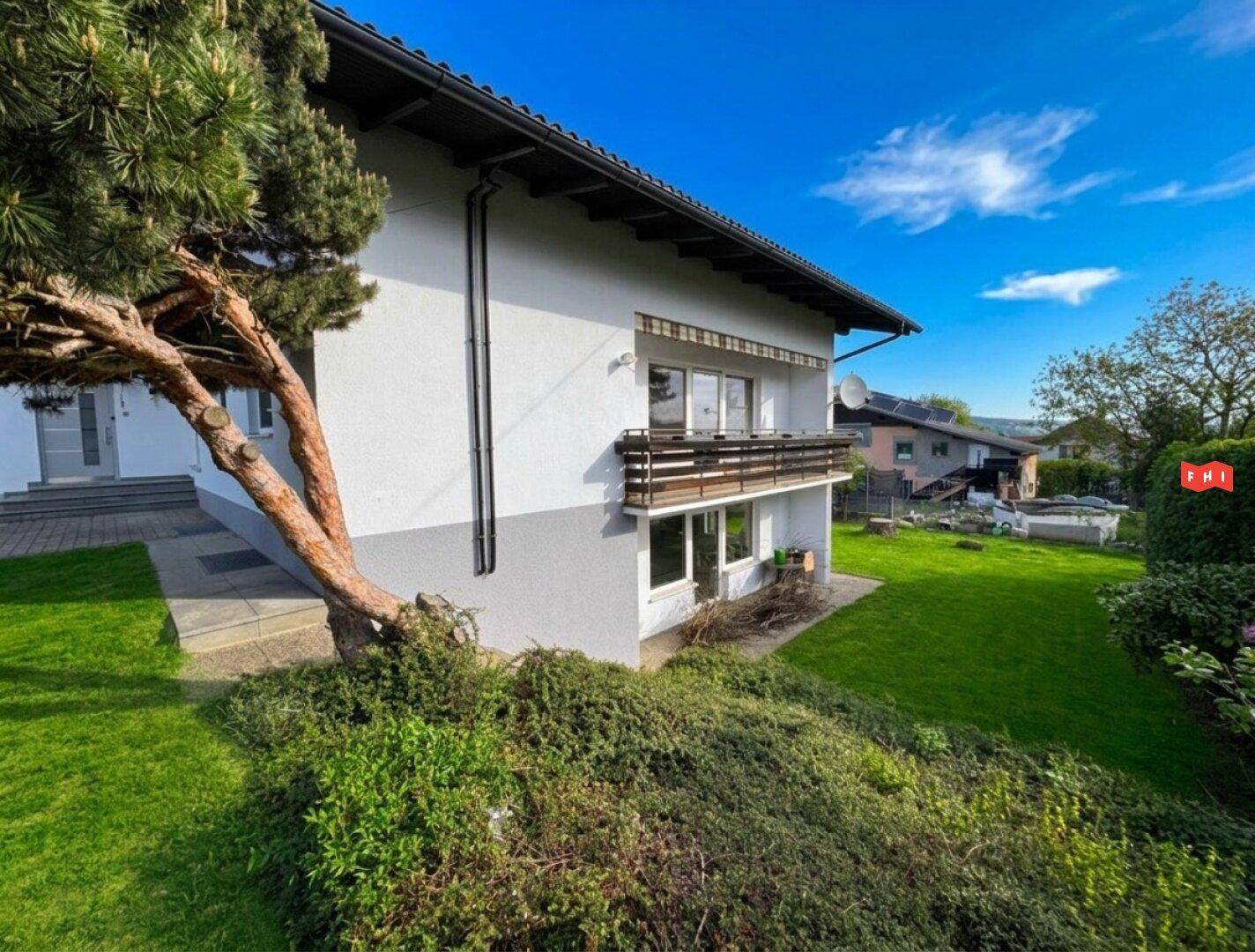 Ansicht des Hauses von der Seite mit Balkon und üppiger Bepflanzung im Gartenbereich.