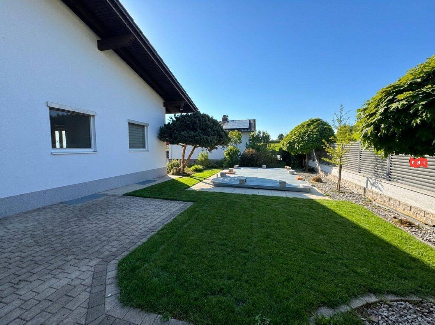 Gepflasterter Bereich neben dem Haus mit Rasenfläche und einem vorbereiteten Poolbereich im Garten.