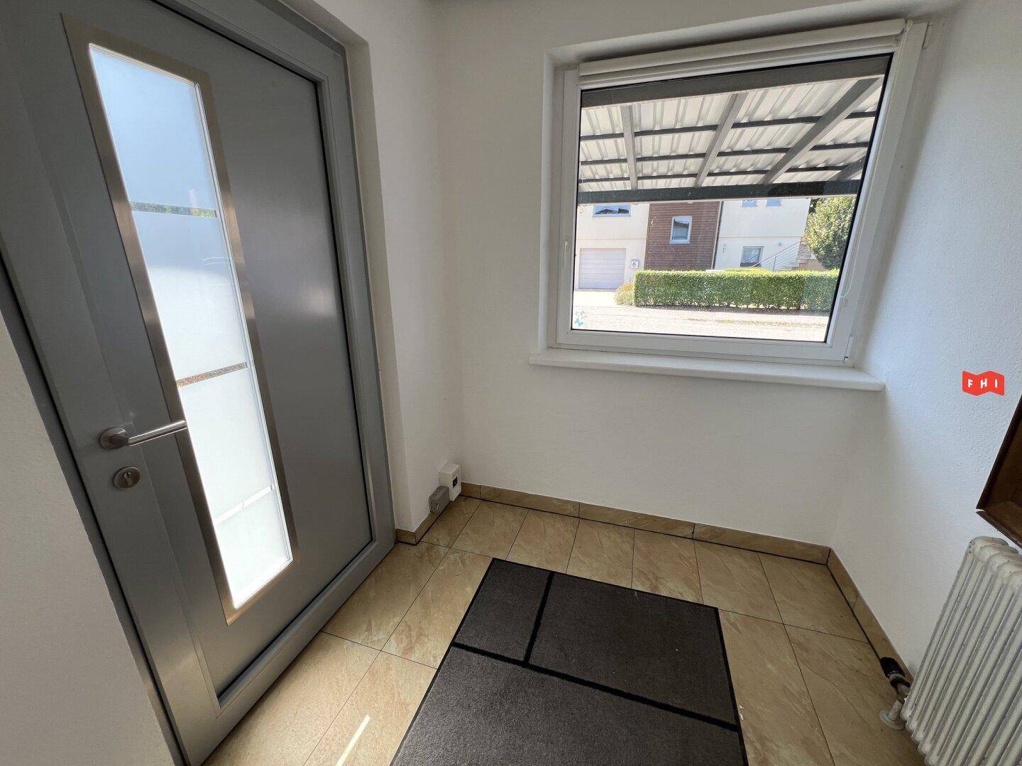 Heller Eingangsbereich mit Fliesenboden, moderner Haustür und Blick nach draußen.