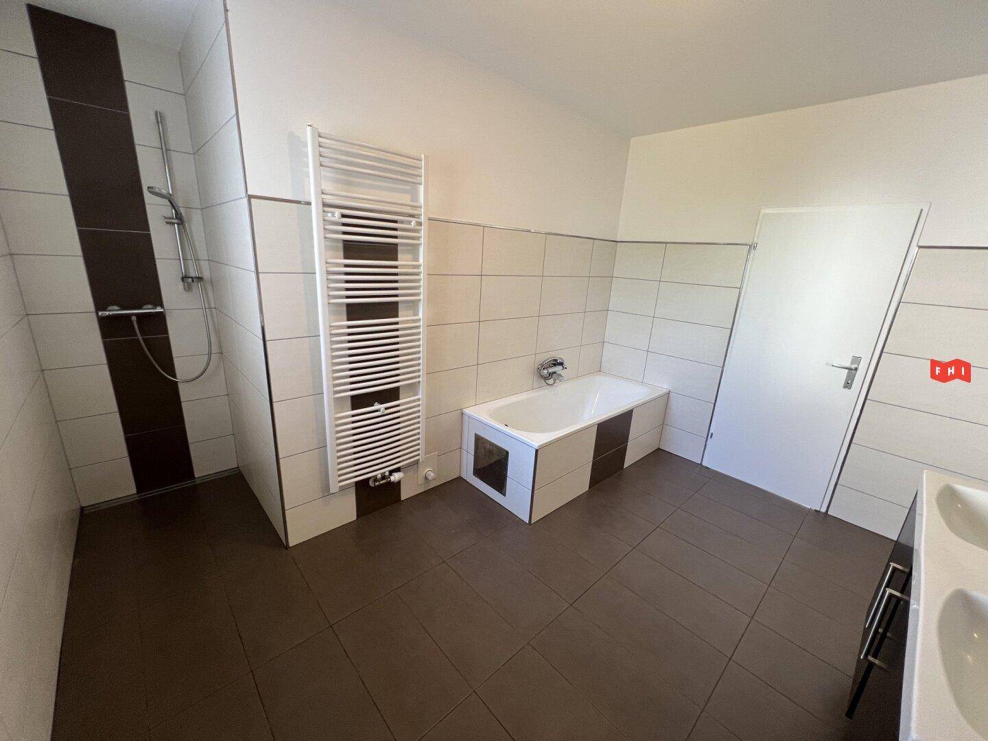 Geräumiges Badezimmer mit Dusche, Badewanne, beheiztem Handtuchhalter und braunen Fliesen.