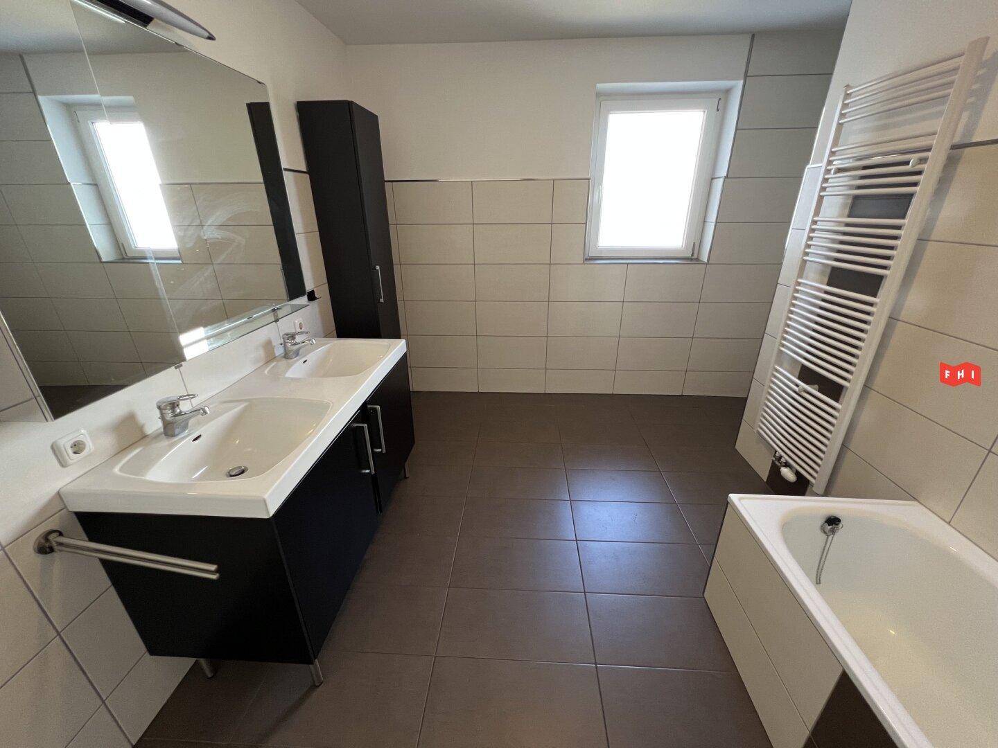Modernes Badezimmer mit Doppelwaschbecken, großem Spiegel, Badewanne und Fenster.