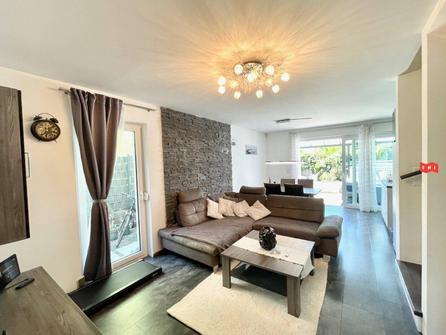 Heller Wohnbereich mit modernem Sofa, dekorativer Steinwand und Blick in den Essbereich.