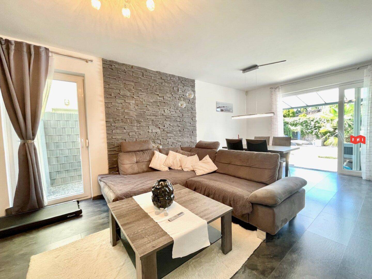 Gemütliches Wohnzimmer mit großem Ecksofa, Steinwand und Zugang zum Garten.