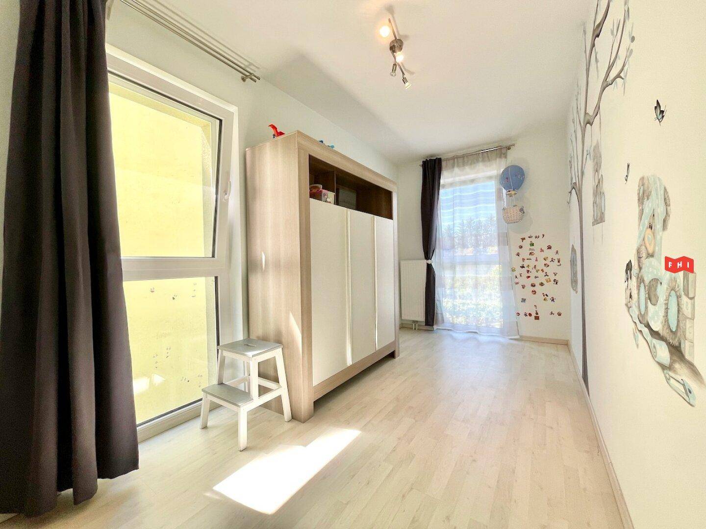 Kinderzimmer mit hellem Laminatboden, großem Fenster und kindgerechter Wanddekoration.