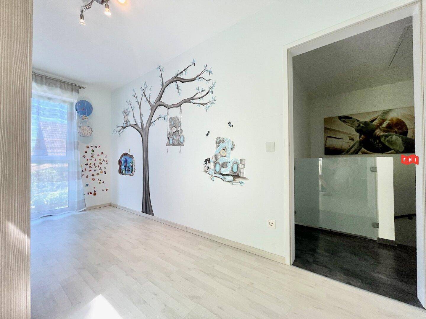 Freundliches Kinderzimmer mit Baum-Wandtattoo und viel Tageslicht durch das Fenster.