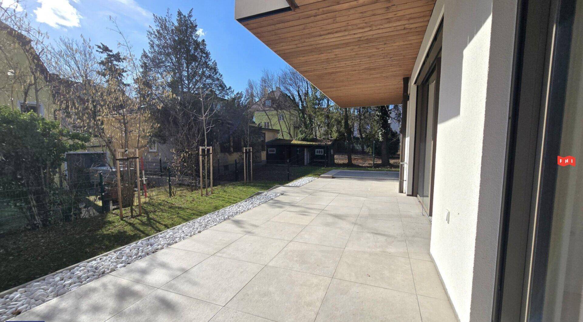 Große, geflieste Terrasse mit angrenzendem Rasenbereich und Bäumen.