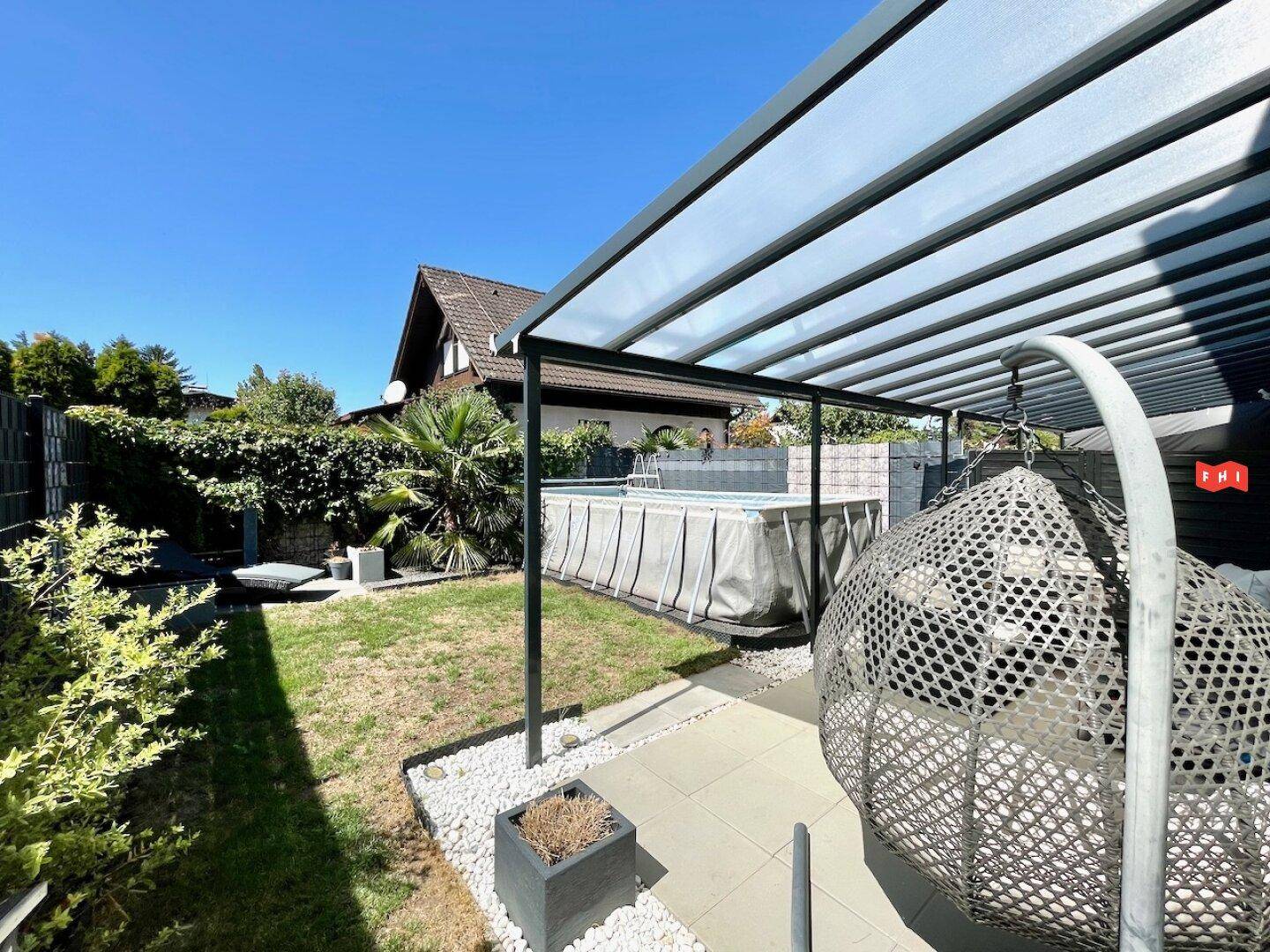 Gepflegter Gartenbereich mit Aufstellpool, überdachter Terrasse und Hängesessel für entspannte Stunden im Freien.