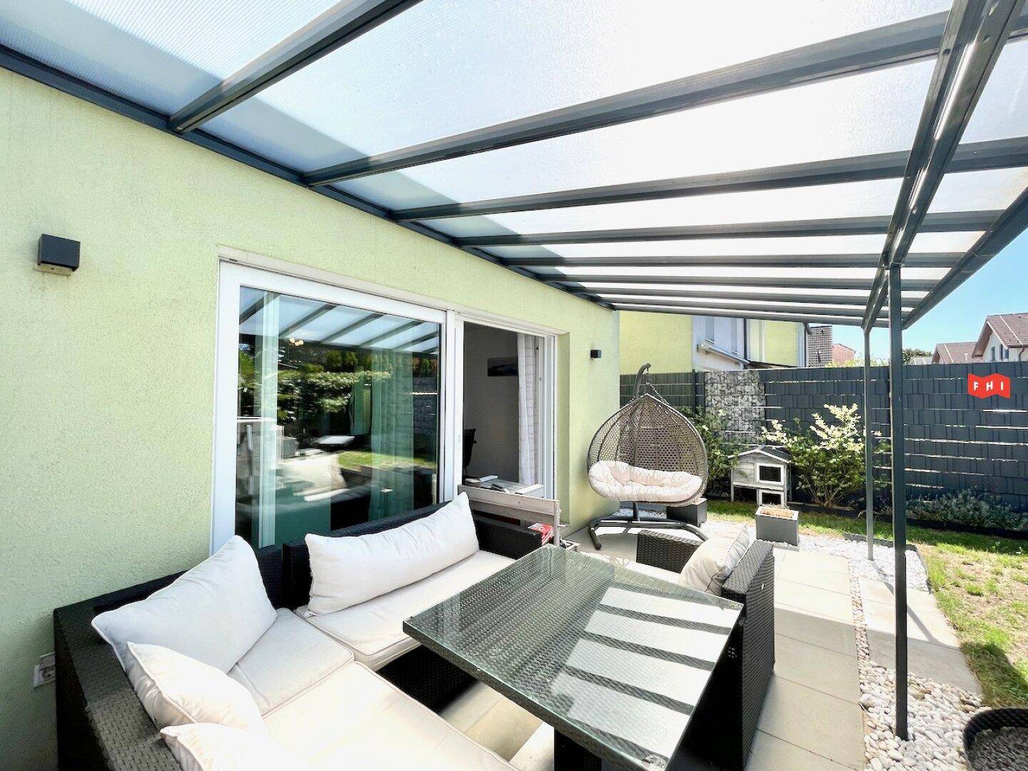 Überdachte Terrasse mit bequemen Loungemöbeln und direktem Zugang zum Garten, ideal für Entspannung im Freien.