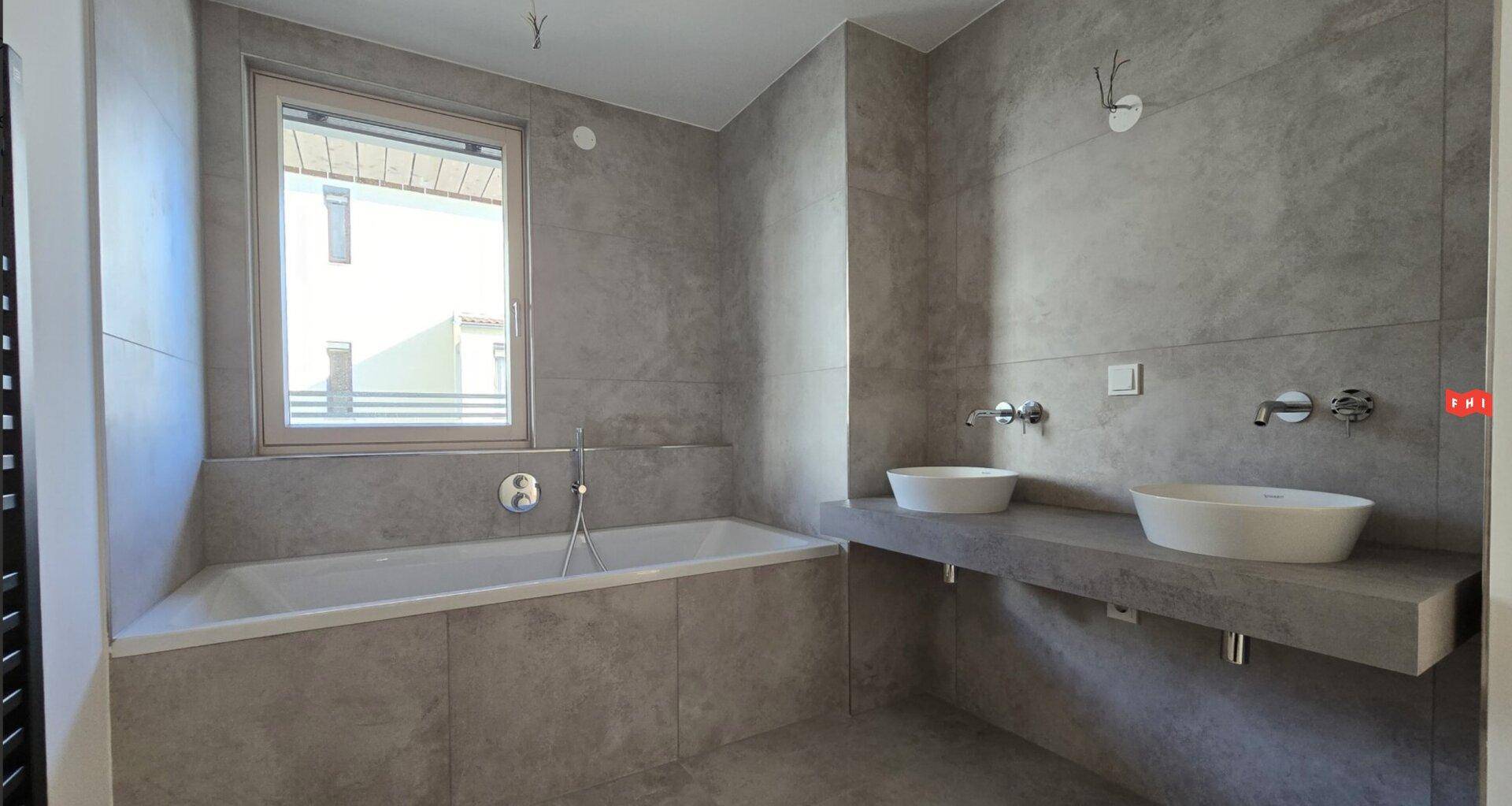 Geräumiges Badezimmer mit Badewanne, Doppelwaschbecken und Fenster.