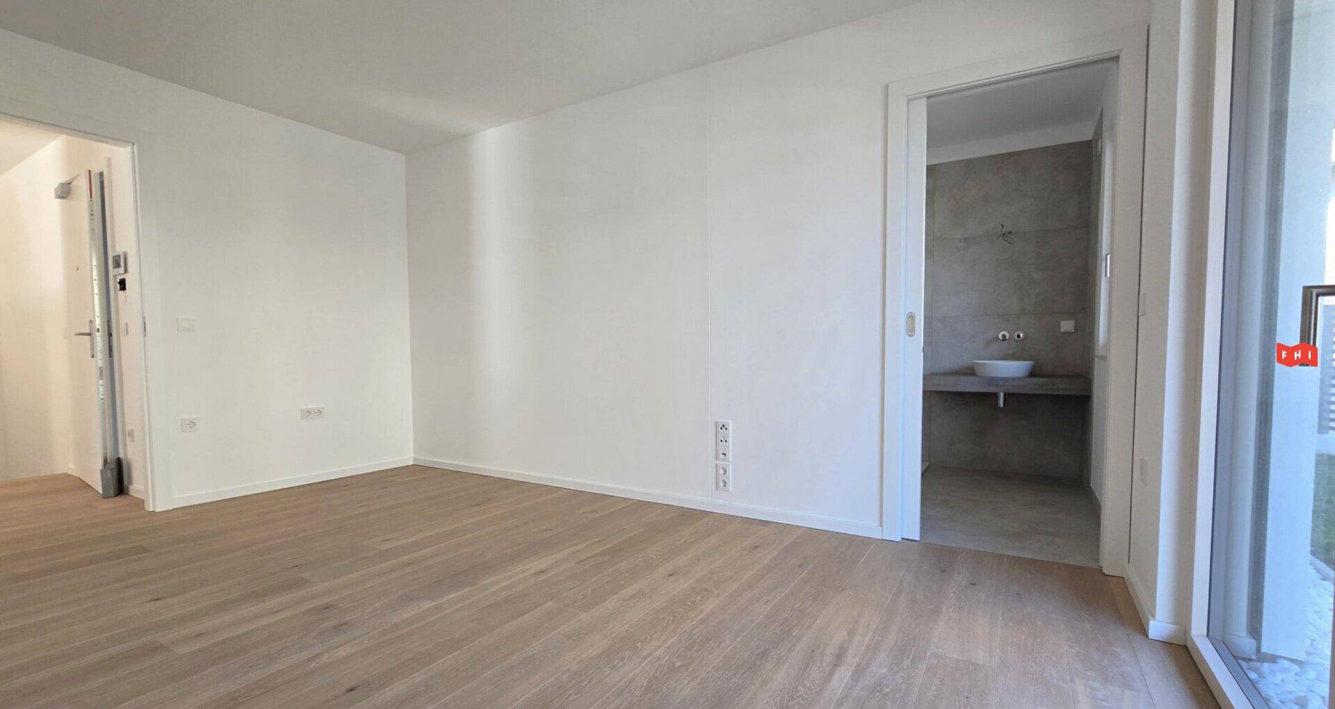 Leeres Schlafzimmer mit Holzboden und Zugang zu einem modernen Badezimmer.