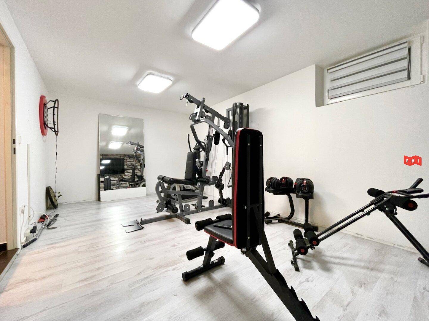 Geräumiger Fitnessraum im Untergeschoss mit verschiedenen Trainingsgeräten und hellem Laminatboden.