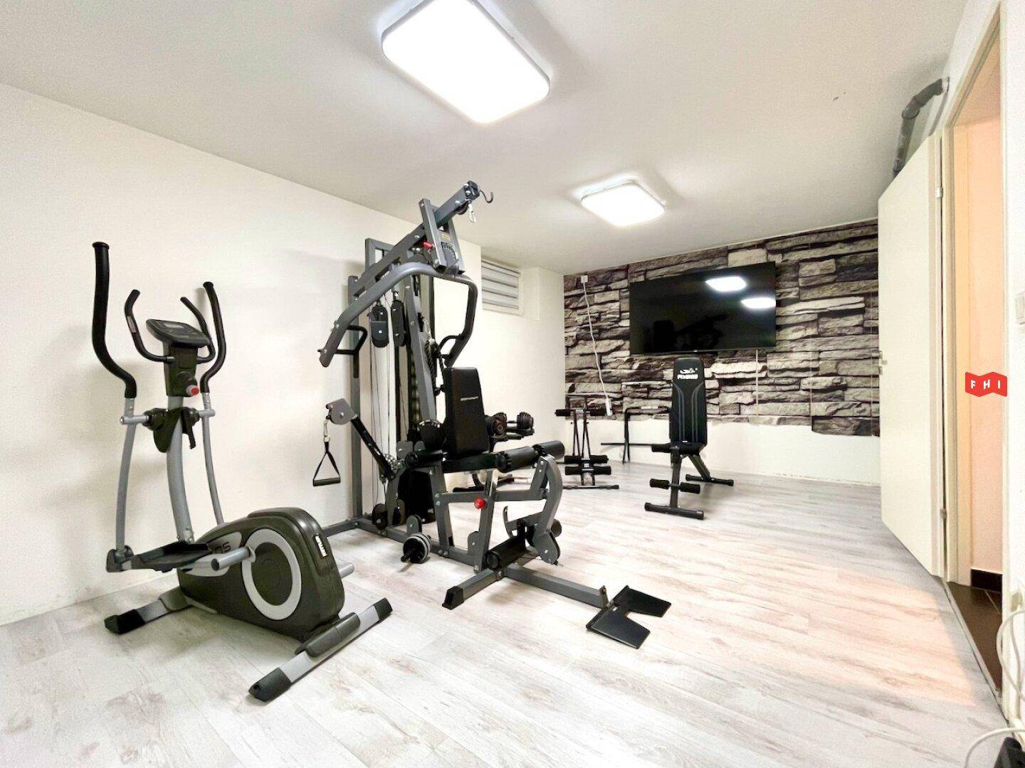 Moderner Fitnessraum mit einer Auswahl an Trainingsgeräten und einer dekorativen Steinwand.