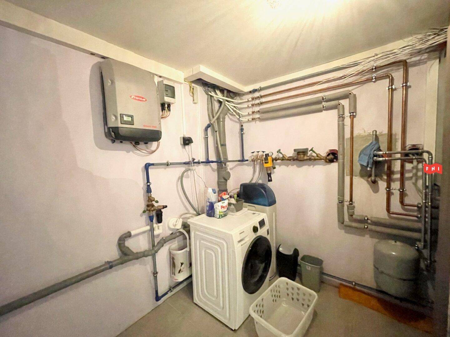 Hauswirtschaftsraum mit Waschmaschine, Trockner und sichtbaren Installationen für Heizung und Wasser.
