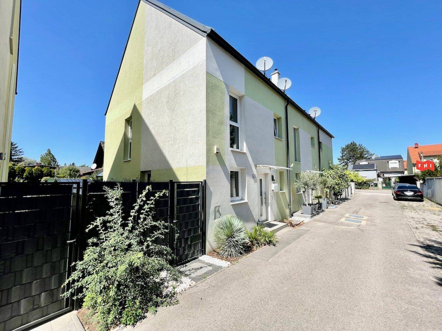 Moderne Reihenhausfassade in hellgrünen und weißen Farbtönen mit gepflegtem Vorgartenbereich.
