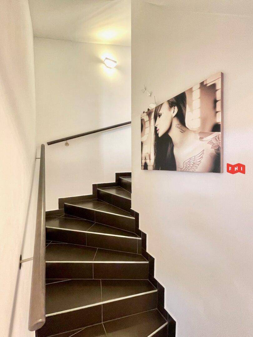 Wendeltreppe mit dunklen Fliesen und Holzgeländer, die die verschiedenen Etagen des Hauses verbindet.