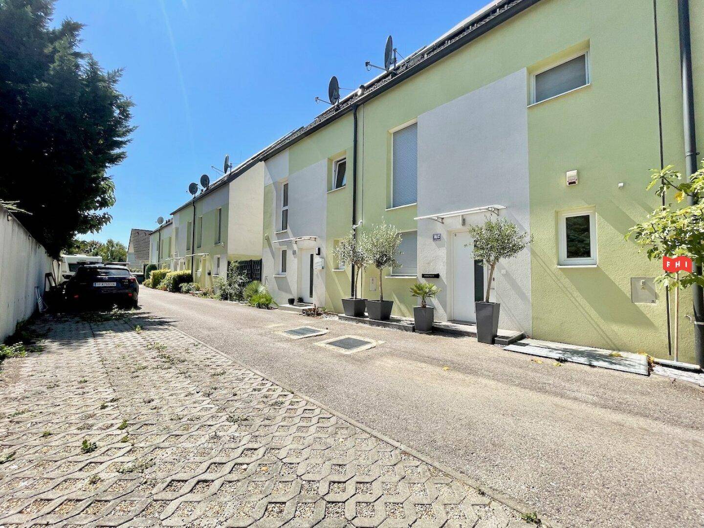 Reihe moderner Reihenhäuser mit hellgrünen und weißen Fassaden entlang einer Zufahrtsstraße.