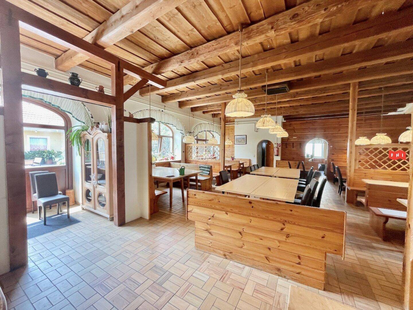 Weiterer Blick in den traditionellen Speisesaal mit Holzbalken, Holzbänken und einem Eingangsbereich.