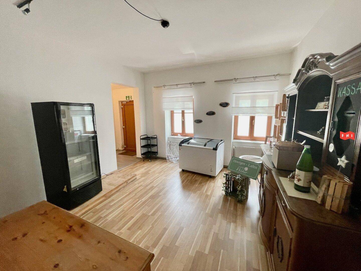 Weiterer Blick in den Verkaufsraum mit mehreren Kühlgeräten, Fenstern und einem Holzboden.