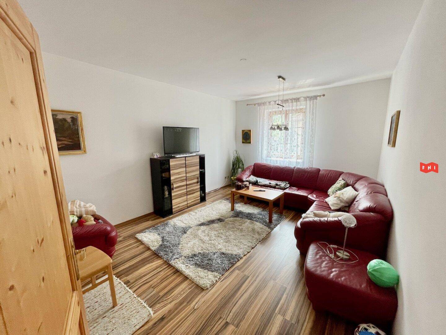 Gemütliches Wohnzimmer mit rotem Ecksofa, Couchtisch, TV-Möbel und Laminatboden.