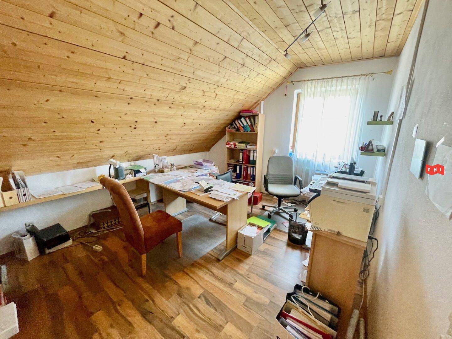 Helles Büro im Dachgeschoss mit schräger Holzdecke, Holzschreibtisch und Regalen, bietet viel Stauraum.