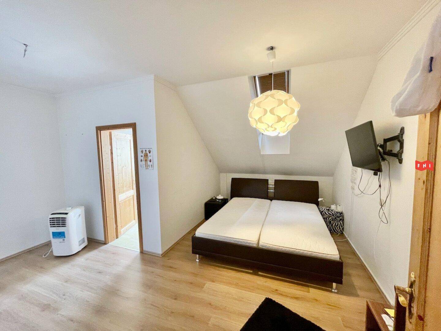 Schlafzimmer im Dachgeschoss mit Doppelbett, Laminatboden und schräger Decke, ausgestattet mit einem Fernseher.