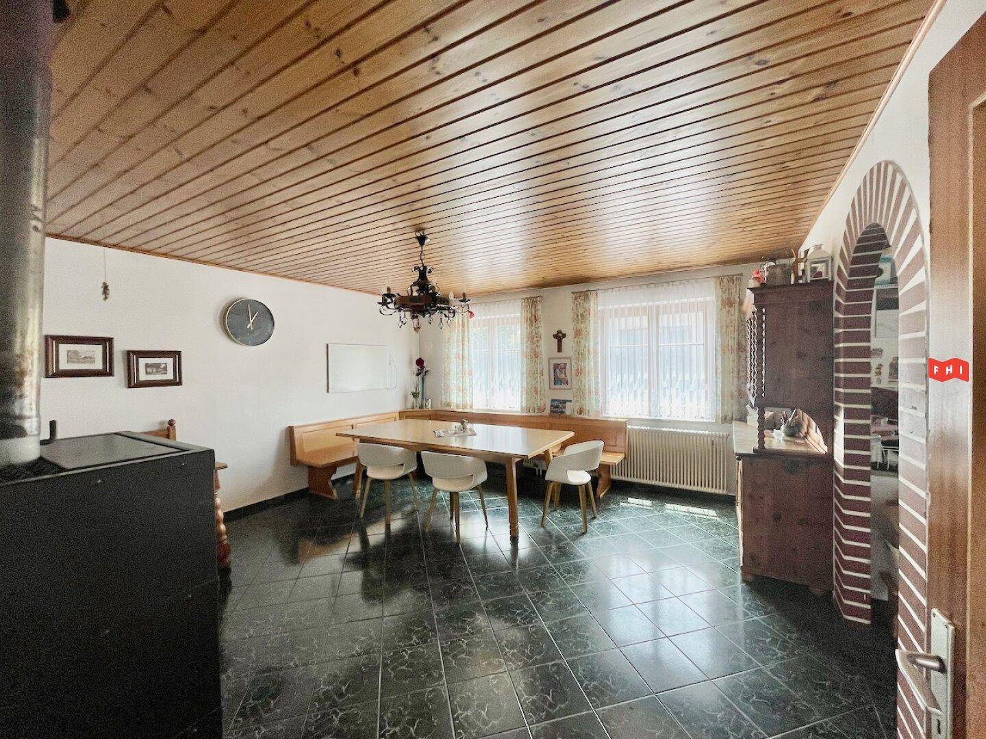 Gemütlicher Essbereich mit Holztäfelung an der Decke, einem Kaminofen und traditionellen Möbeln.