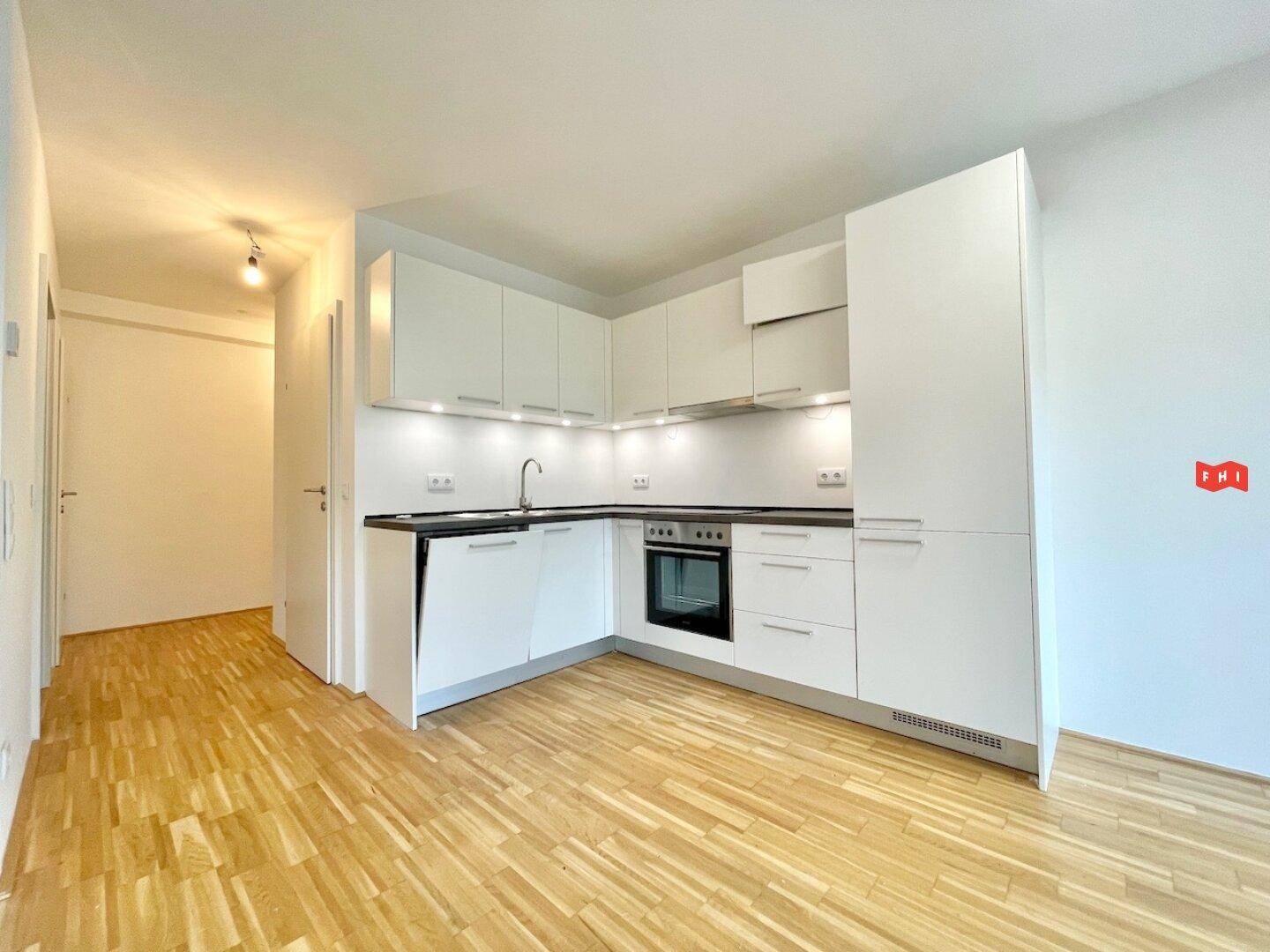 Moderne Einbauküche mit weißen Schränken und dunkler Arbeitsplatte, offen zum Wohnbereich.