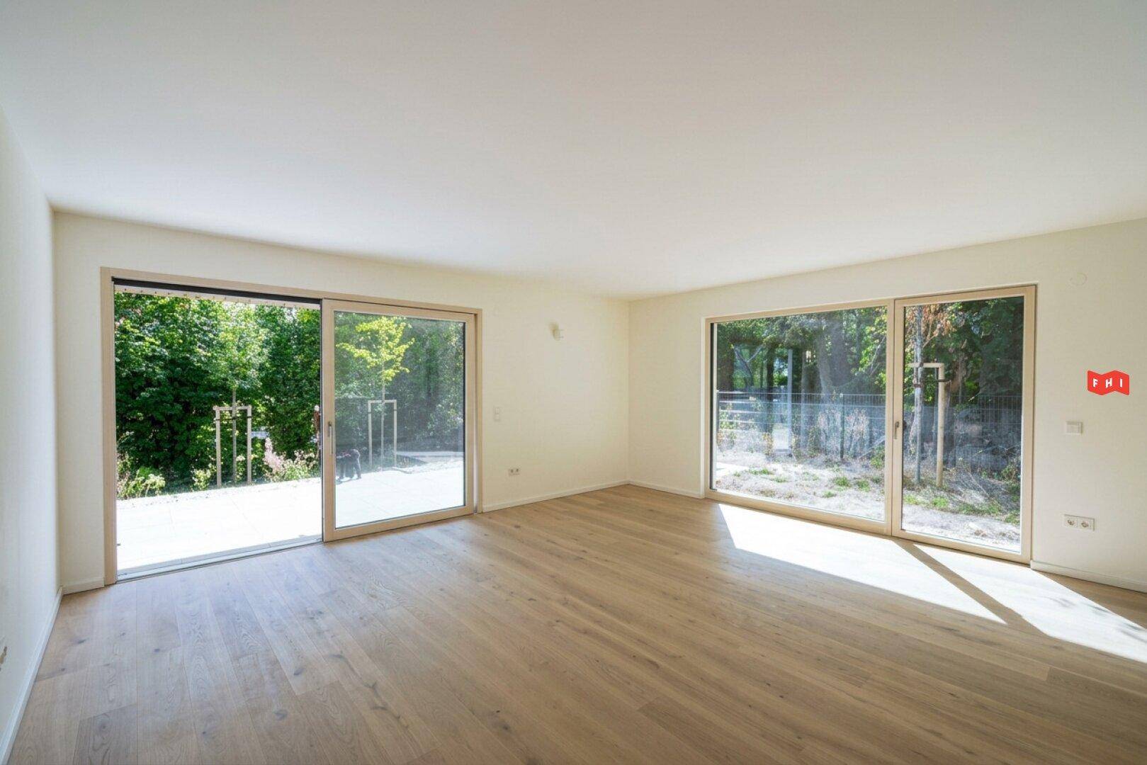 Helles, leeres Zimmer mit Holzboden und großen Schiebetüren zur Terrasse.