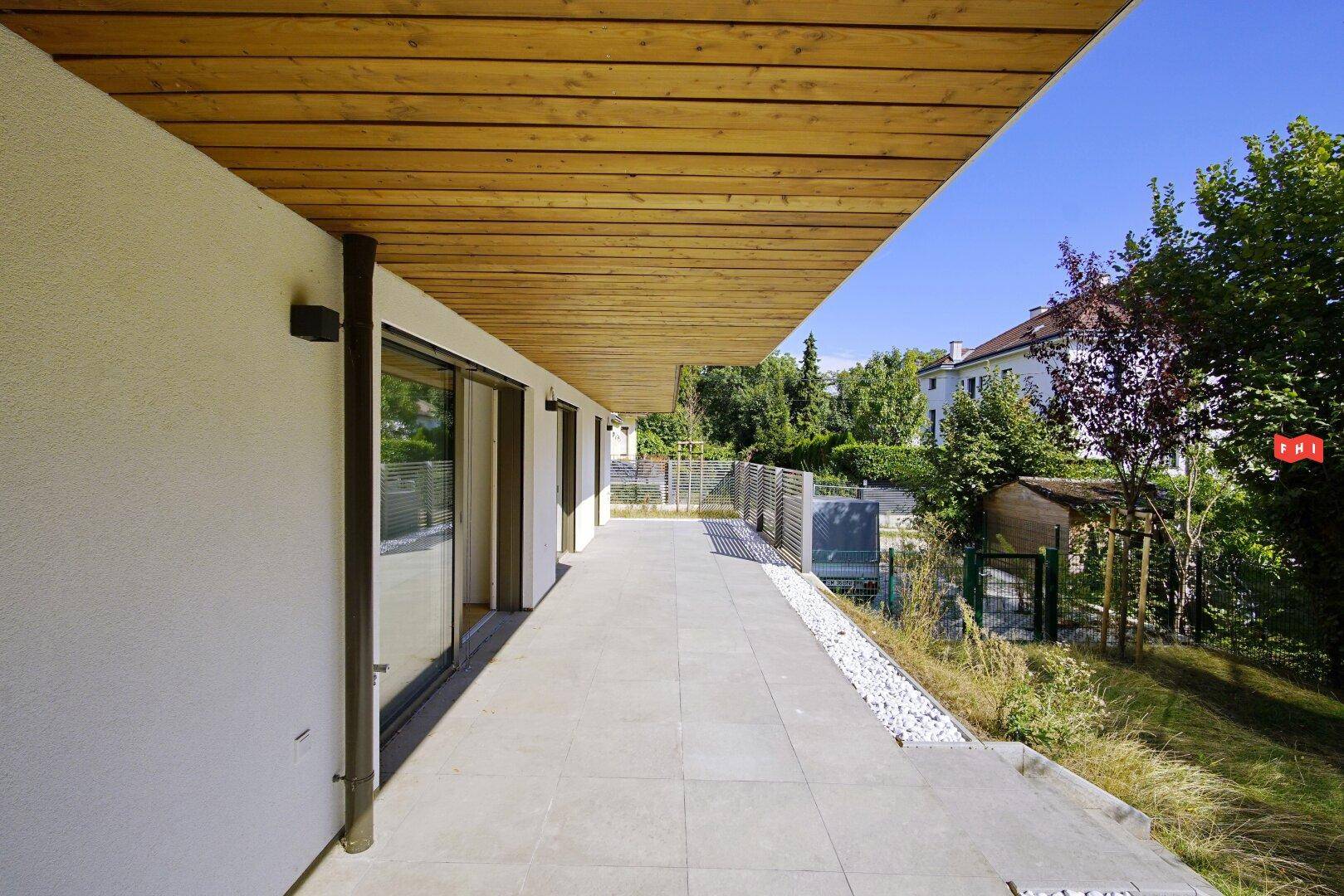 Lange, geflieste Terrasse mit Holzdecke und Blick ins Grüne.