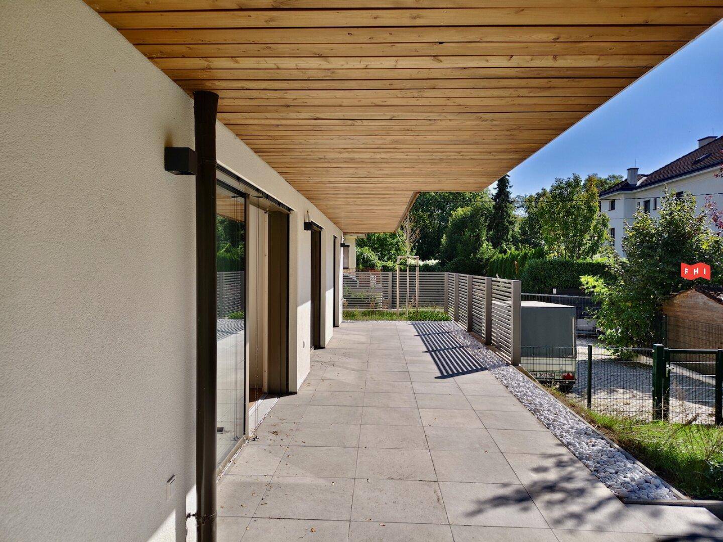 Lange, geflieste Terrasse mit Holzdach und Blick auf die grüne Umgebung des Hauses.