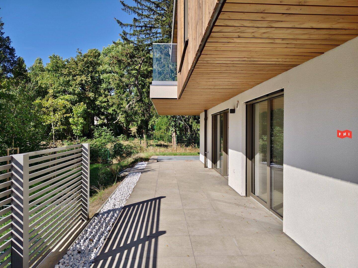Geräumige Terrasse mit Fliesenboden und Holzdach, umgeben von viel Grün und Bäumen.