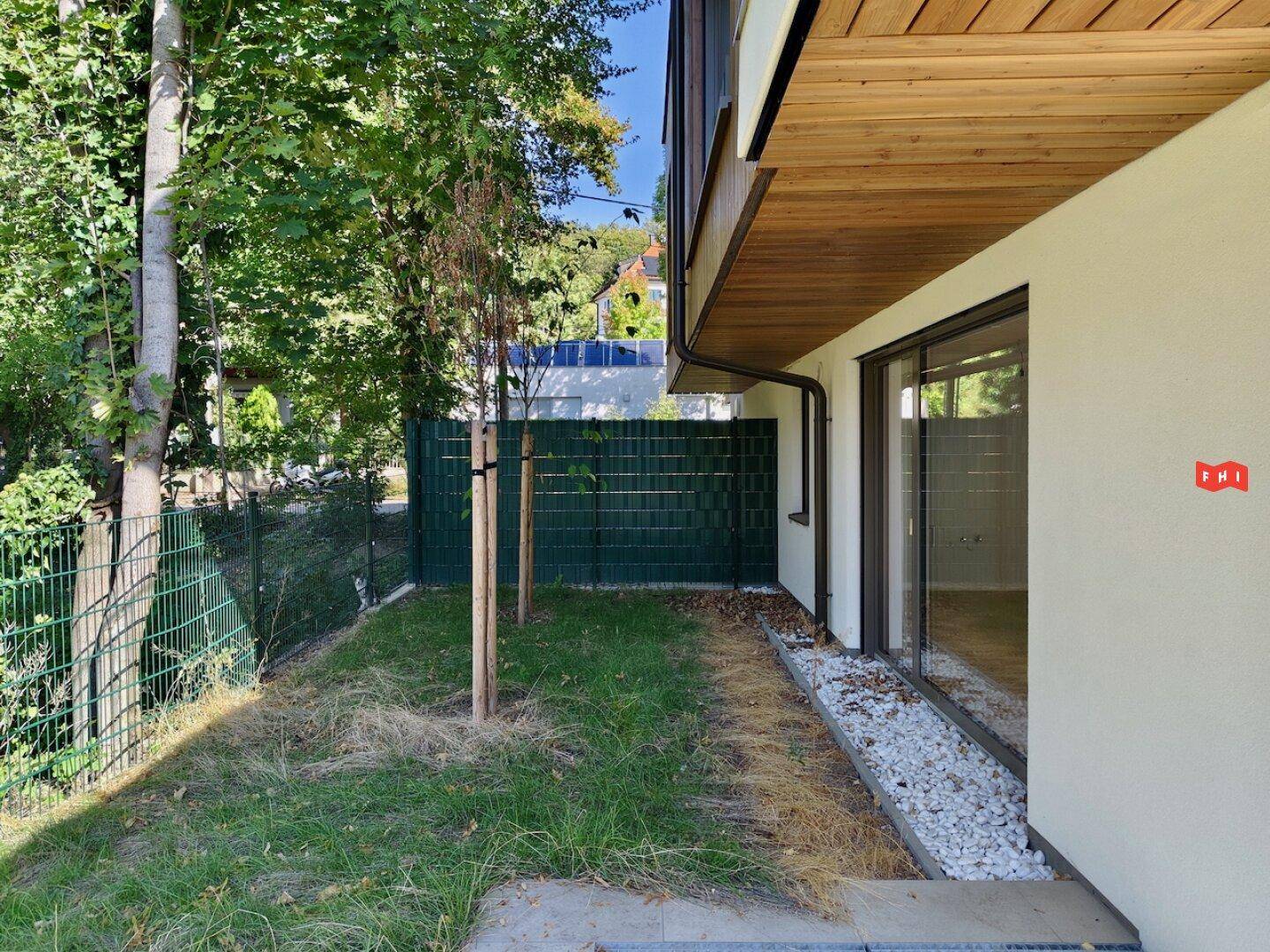Kleiner Gartenbereich mit Zaun und jungen Bäumen neben dem modernen Wohnhaus.