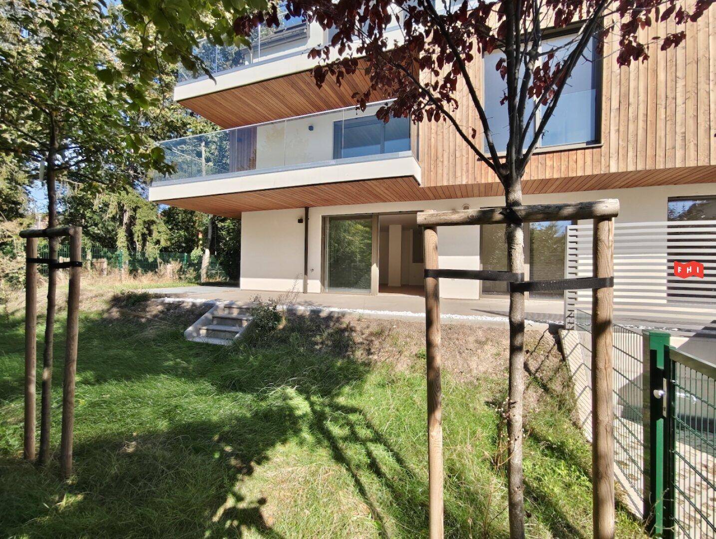 Gartenbereich mit jungen Bäumen und Zugang zu einer Terrasse im Erdgeschoss des Neubaus.
